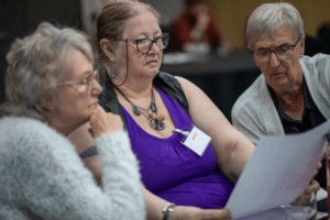 Three adults sitting together at a table, reading and discussing a document during the Bernicia Tenant Engagement Event.
