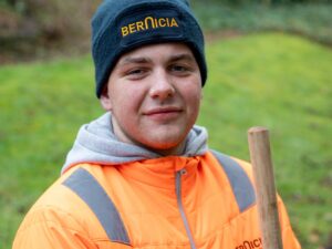 Bernicia Estate Services colleague wearing an orange high-visibility jacket and branded beanie while working outdoors.